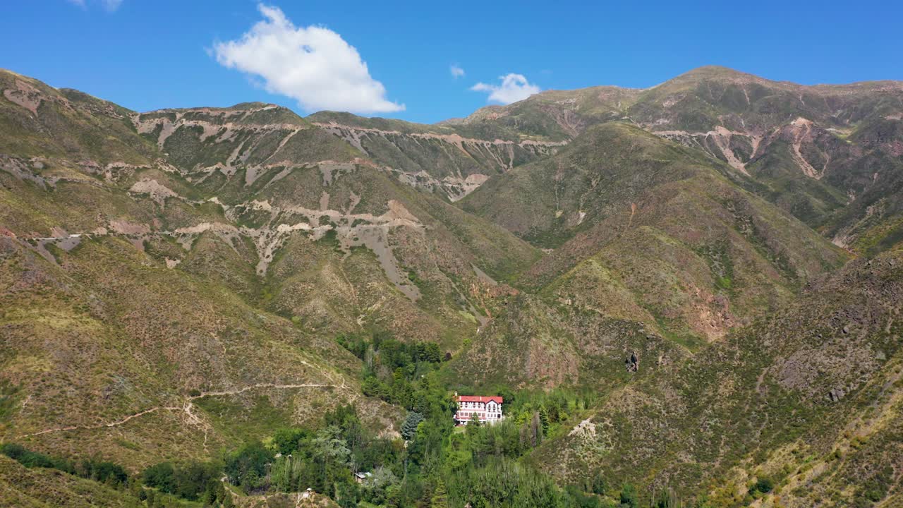 drone volando hacia un hotel rural en medio de un valle montañoso en un día soleado