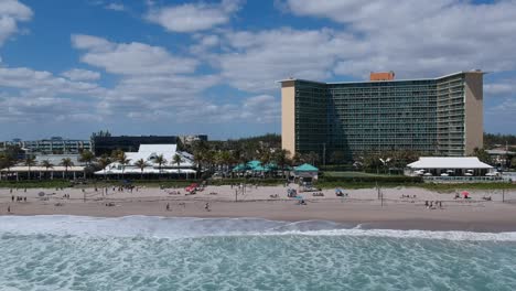 Volando-Lejos-De-Restaurantes-Y-Un-Gran-Condominio-En-La-Playa-Con-Olas-Moviéndose-Hacia-La-Orilla