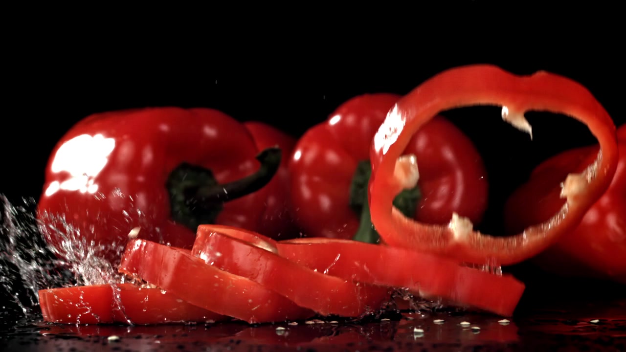 Nakrájená červená paprika padající zpomaleně s cákanci vody