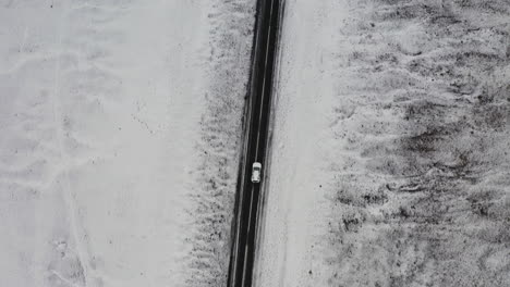 aerial: top down follow shot of one car driving on a snowy road in iceland