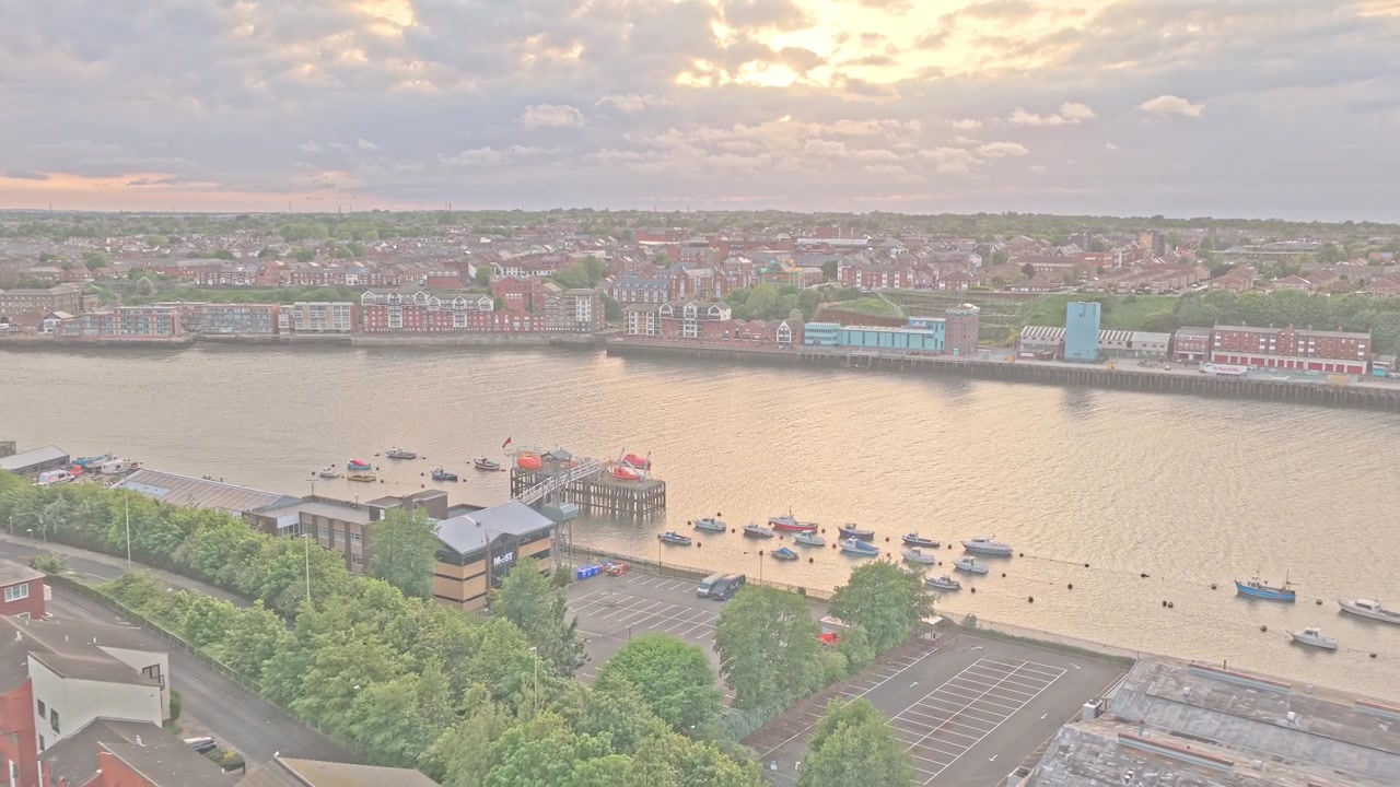 Un drone vola in avanti sopra il Forte Romano di Arbeia che si affaccia sul fiume Tyne a South Shields, Tyne and Wear, Inghilterra, rivelando lo sviluppo lungo il fiume, barche ormeggiate e il lungomare opposto, con un sorvolo in avanti