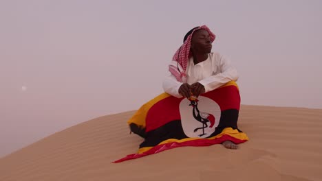 african young man holding flag of uganda in desert