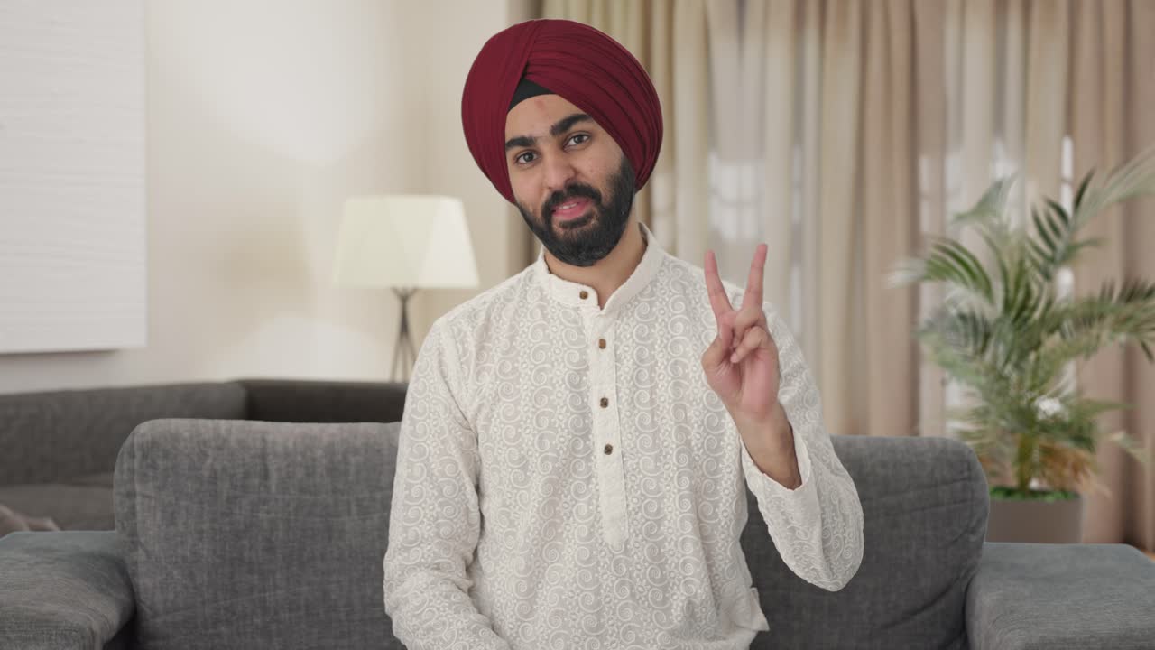 Uomo indiano Sikh felice che mostra il segno della vittoria