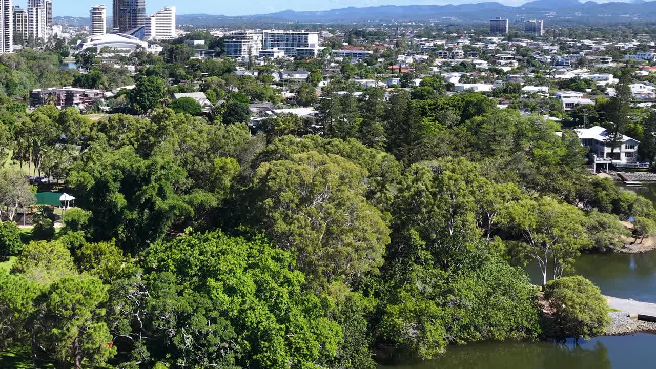 高層ビル群、運河、そして生い茂る緑の木々が特徴の、晴れた郊外の風景を捉えたドローン映像。