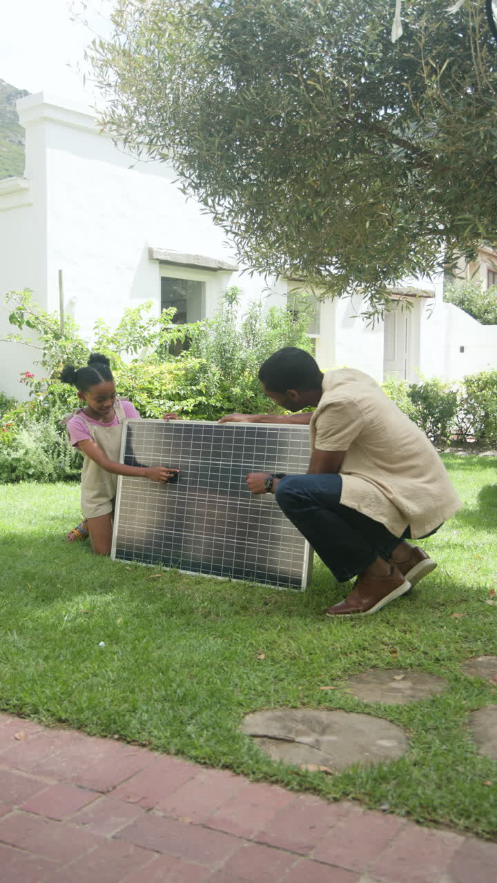 Vertical video: Father and daughter installing solar panel in garden, enjoying sustainable living