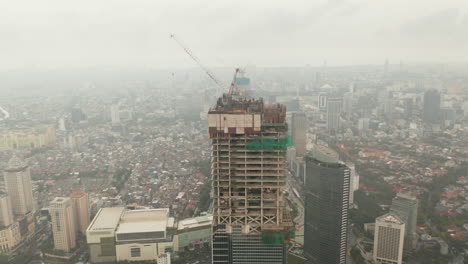 Aerial-dolly-shot-tilting-into-overhead-of-tall-skyscraper-under-construction-in-urban-city-center