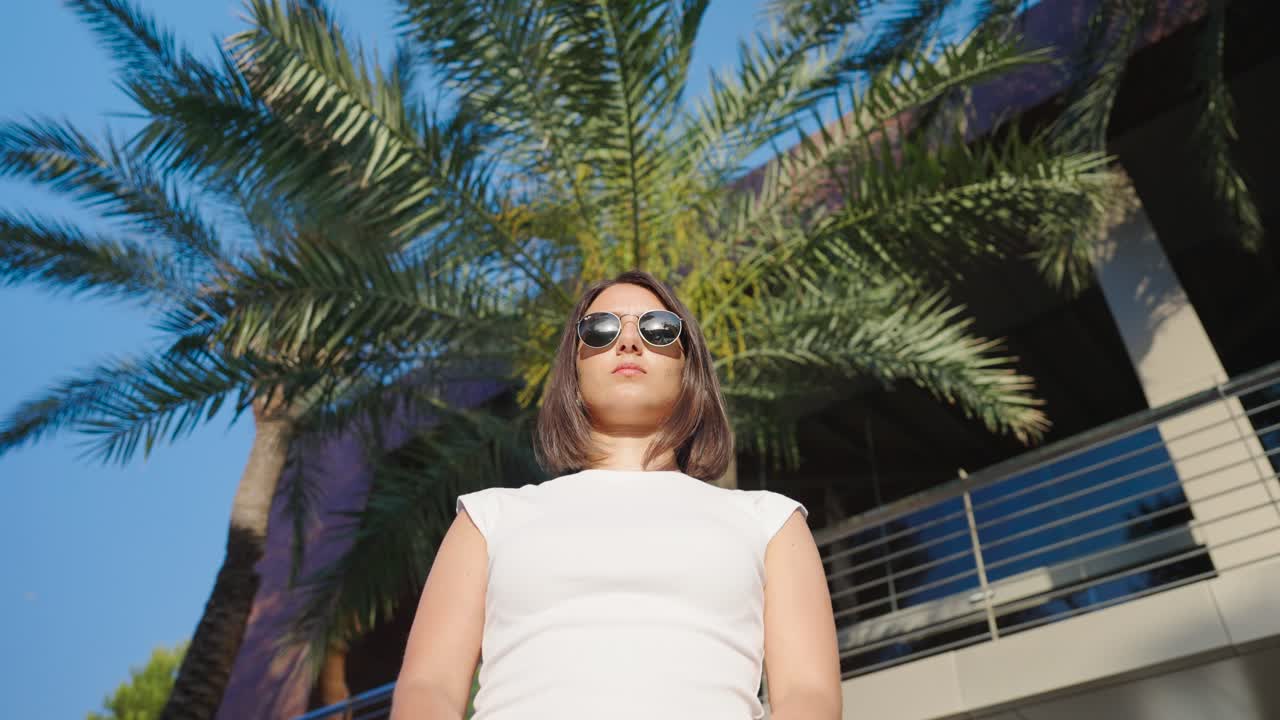 A woman wearing sunglasses standing in front of a palm tree