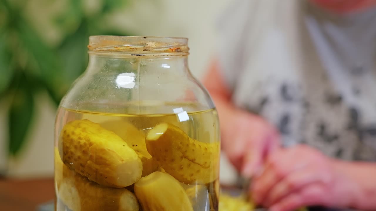Primer plano de un tarro de cristal lleno de pepinillos en vinagre durante la tranquila preparación de comida casera