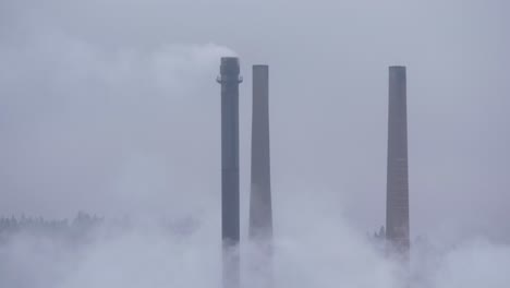 las chimeneas de la fábrica de papel emiten una chimenea a la atmósfera en un día frío y nublado - primer plano largo