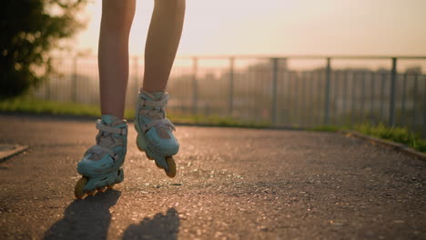 primer plano de las piernas de la dama usando patines de ruedas mientras patina al aire libre, con la luz del sol brillando detrás creando sombras dramáticas en el pavimento, y una barandilla de hierro borrosa con vista del paisaje urbano en el fondo
