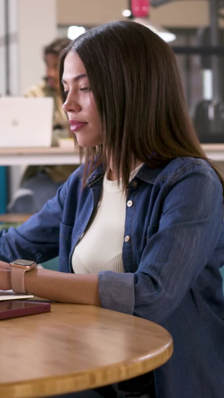 Video verticale: Donna in camicia di jeans che guarda a sinistra, usa il telefono e i documenti in ufficio per completare un'attività.