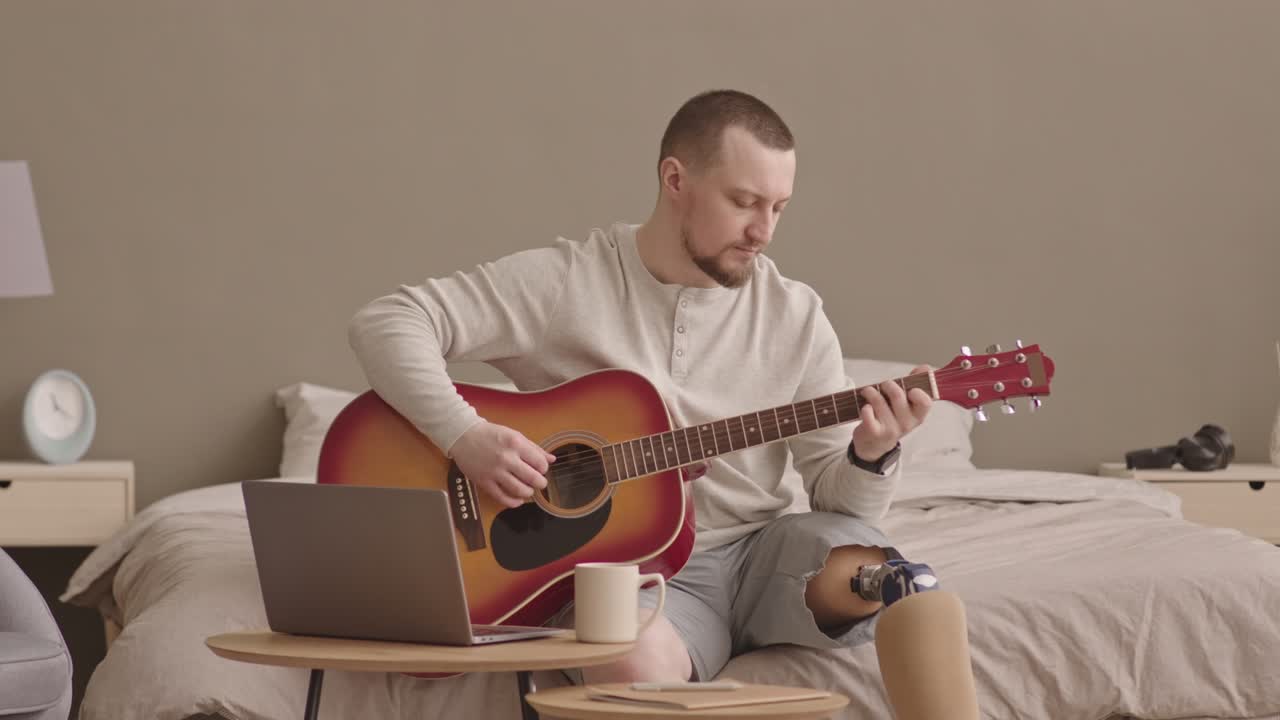 человек с протезом на ноге учится играть на гитаре дома