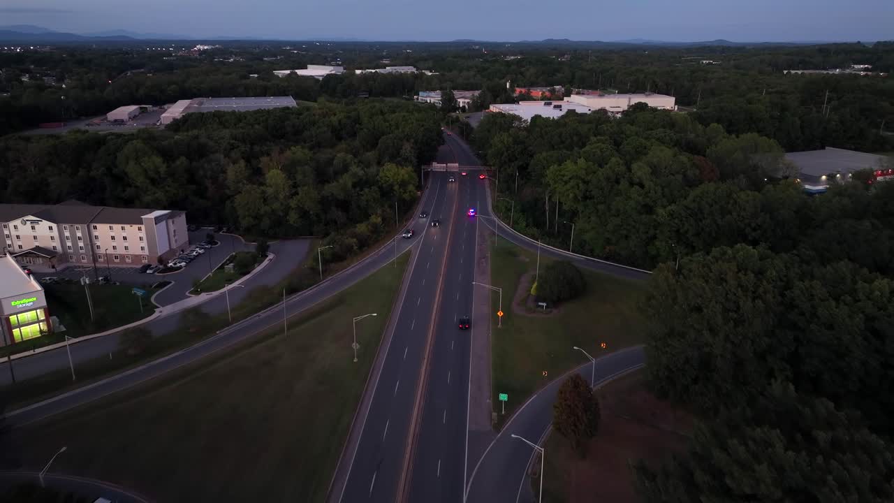 Drone following shot of fast police car on suburb road at dusk Green forest trees in suburb. American town in USA. Aerial tracking wide shot