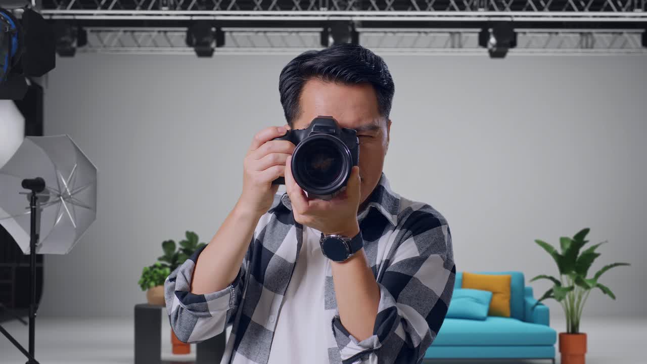 スタジオに立ち、カメラで写真を撮りながら笑顔のアジア人写真家のクローズアップ