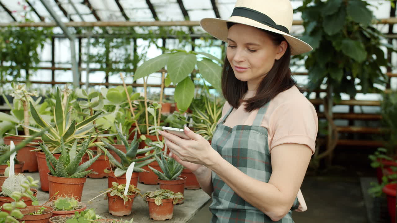 Woman in greenhouse checking plants on her phone