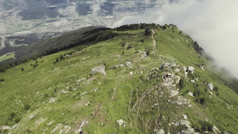 aerial drone shot of a grass covered mountain top, lagoz with a small trail leading up with clouds around