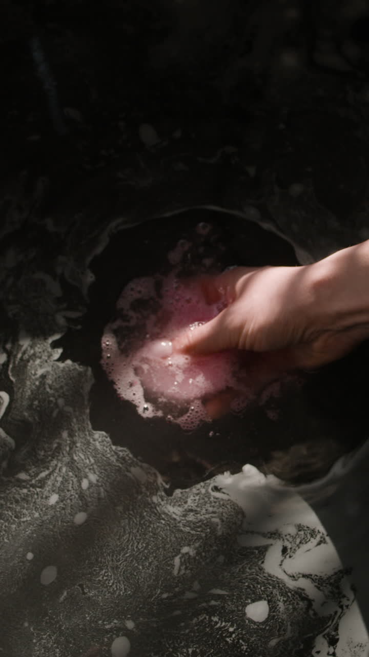 Hand holding a pink bath bomb in a bath