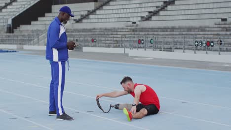 Diverse-male-coach-and-disabled-athlete-with-prosthetic-leg-training-and-stretching