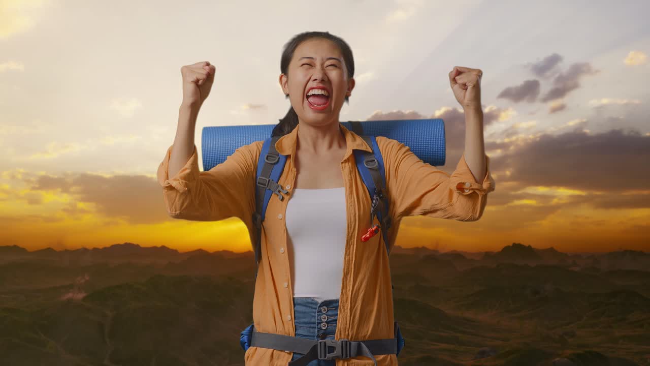 excursionista asiática con mochila de montañismo gritando meta celebrando el éxito mientras está de pie en la cima de la montaña durante la hora del atardecer