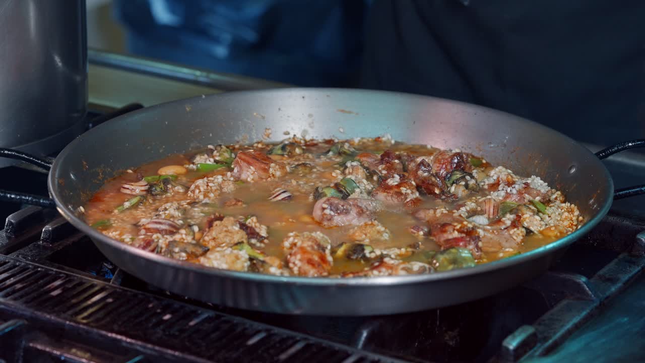 주방장이 고기와 야채를 곁들인 스페인 빠에야에 국물을 붓는다