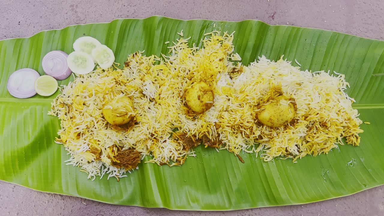 A fluffy mound of aromatic biryani rice, white and golden, rests on a rustic wooden table, evoking warmth, with grains spilling over the edge.