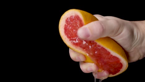 Eine-Rote,-Saftige-Grapefruit-Mit-Weißer-Hand-Vor-Schwarzem-Hintergrund-Auspressen