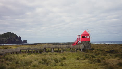 Static-wide-shot-of-small-red-windmill-located-at-the-rocky-coastline