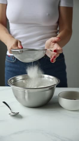 woman sifting flour into a mixing bowl