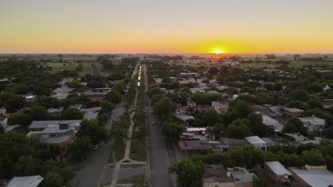 dolly in flying over boulevard main street and santa elisa countryside town houses at sunset with bright sun setting in the horizon, entre rios, argentina