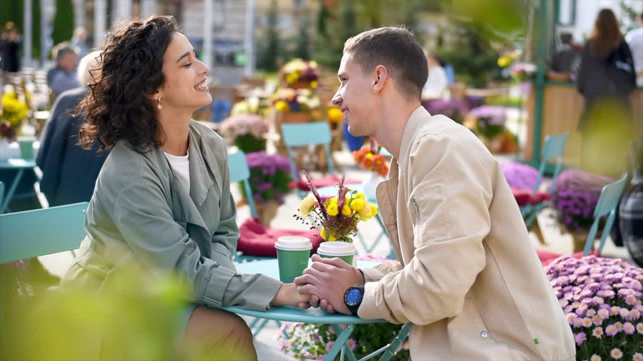 A romantic couple outdoors near a cafe. Holding hands, kissing, flowers on the table. Autumn atmosphere. Slow motion