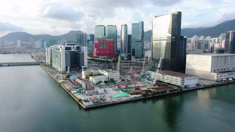 área-De-La-Bahía-De-Hong-Kong-Kowloon-Con-Rascacielos-De-La-Ciudad-Y-Nuevo-Edificio-Del-Hospital-Infantil-Durante-La-Construcción,-Vista-Aérea