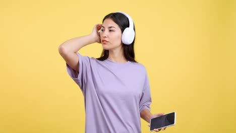 young woman enjoying music with headphones on a yellow background