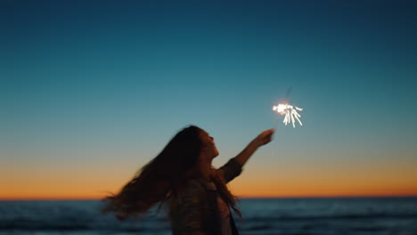 mujer bailando con bengalas en la playa al atardecer celebrando la víspera de año nuevo niña divirtiéndose bailando con fuegos artificiales disfrutando de la celebración del día de la independencia junto al mar