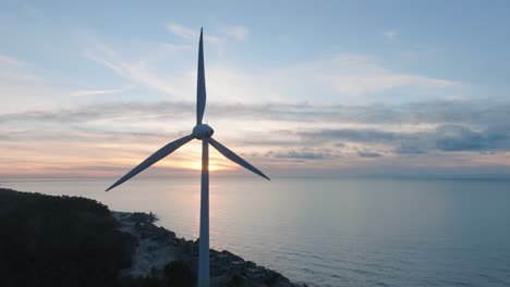 Aerial-view-of-abandoned-seaside-fortification-buildings-at-Karosta-Northern-Forts-on-the-beach-of-Baltic-sea-in-Liepaja,-sunset,-golden-hour,-spinning-wind-turbine,-wide-drone-dolly-shot-moving-left