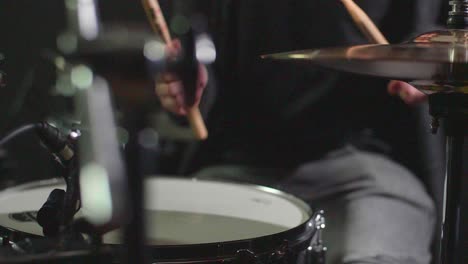 smooth slow motion of a drum set being played in front of a dark background while camera makes a panning gimbal movement