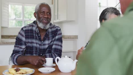 Dos-Parejas-De-Ancianos-Diversas-Sentadas-Junto-A-Una-Mesa-Bebiendo-Té-Juntas-En-Casa