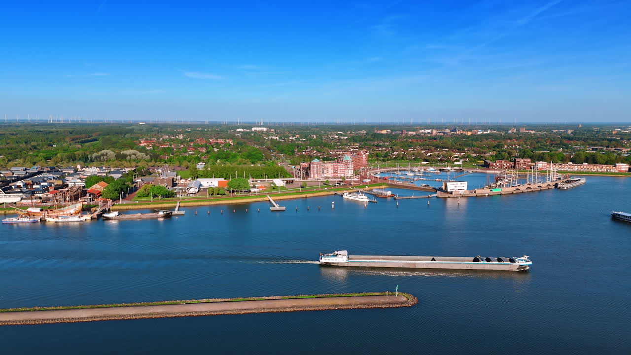 Ferryboat moving by the water along the dike. Sunny scenery of Lelystad, the Netherlands at backdrop. Aerial view.