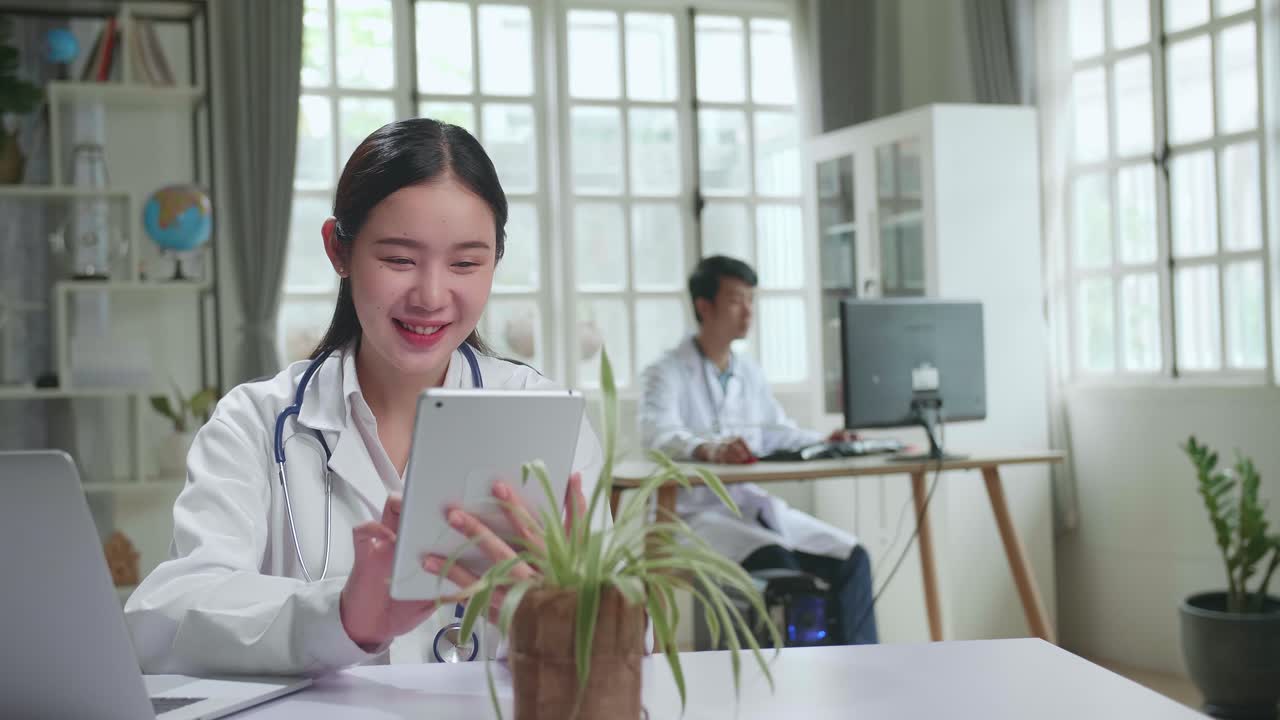 Young Asian Woman Doctor Is Using Tablet While Work With Laptop Computer In Workplace. Medical Concept
