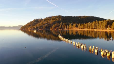 Evening-Sunset-Drone-Aerial-Over-Glenbrook,-Lake-Tahoe,-Nevada,-With-Old-Pier-Pilings-Coming-Out-Of-Calm-Water