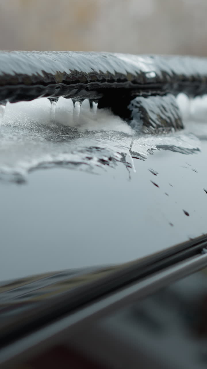 얼음과 눈의 두꺼운 층으로 인 자동차 지붕의 클로즈업, 검은 금속 레일의 가장자리를 따라 매달린 아이스클을 특징으로합니다. 흐릿한 겨울 도시 배경