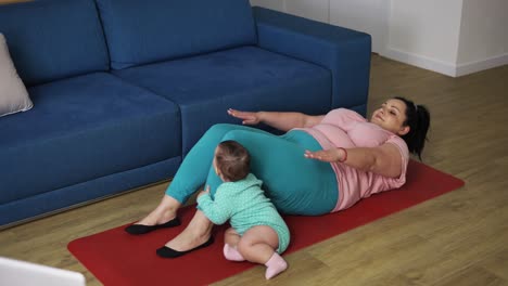 overweighted woman doing abdominal exercises while her baby playing next to her