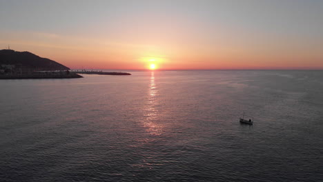 early morning drone shot with one fishing boat surrounded by serene waves near coastline city with mountain range skyline