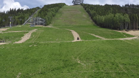 tracking aerial 4k shot of a four wheeler driving up a green slope in the mountains of dolní morava, czechia, heading towards the sky walk attraction between forests