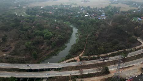 Aerial view of a highway and bridge spanning a river, with a village and natural landscape