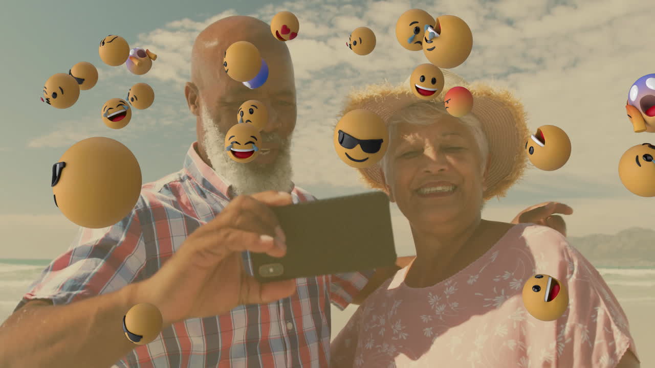 Elderly couple taking selfie surrounded by floating emoji animations on beach