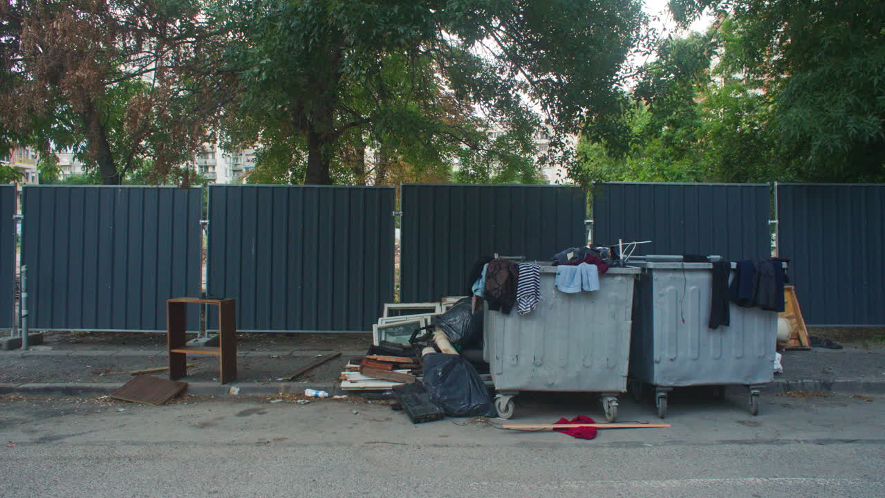 Abandoned construction materials, wood, furniture, frames, windows, clothes and filled bags near a dumpster in Sofia, Bulgaria