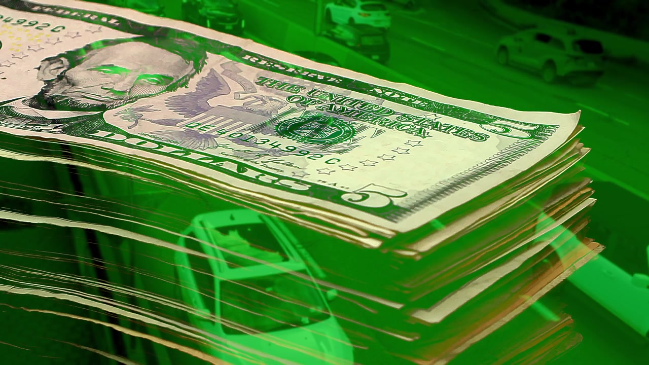 Green-toned double exposure of growing US dollar banknotes stack over busy highway traffic. Conceptual metaphor for capital growth, profitable transport, rising income, and prosperity.
