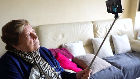 mujer anciana usando un palo de selfie con un teléfono inteligente en casa