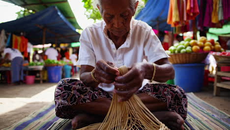 elderly woman weaving a basket at a market