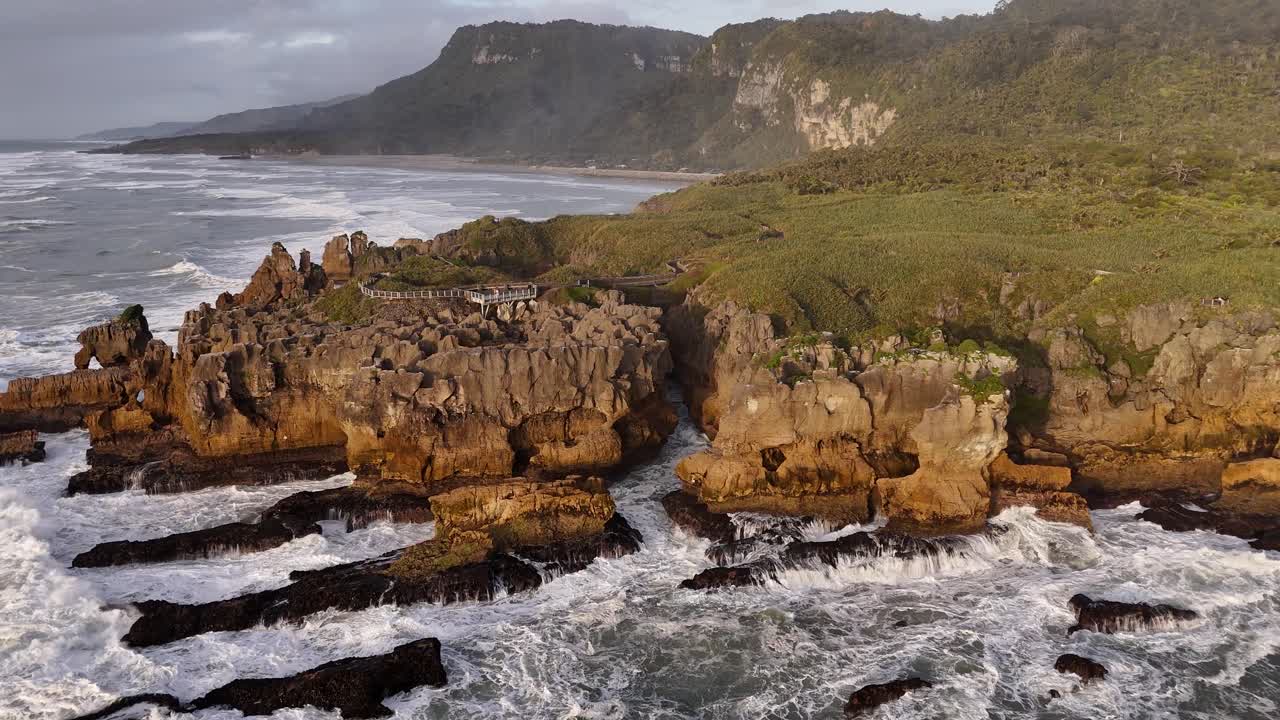 Veduta aerea al tramonto dorato delle Pancake Rocks a Punakaiki, sull'Isola del Sud della Nuova Zelanda, con le onde che si infrangono lungo le aspre scogliere calcaree e una luce calda che illumina il drammatico paesaggio della costa occidentale